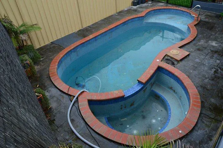 Old outdated leaking swimming pool with rust problems and hollow brick coping, pool tiles falling off and the quartzon is delaminating.
